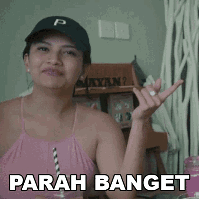 a woman wearing a pink tank top and a black hat with the word parah banget written on it