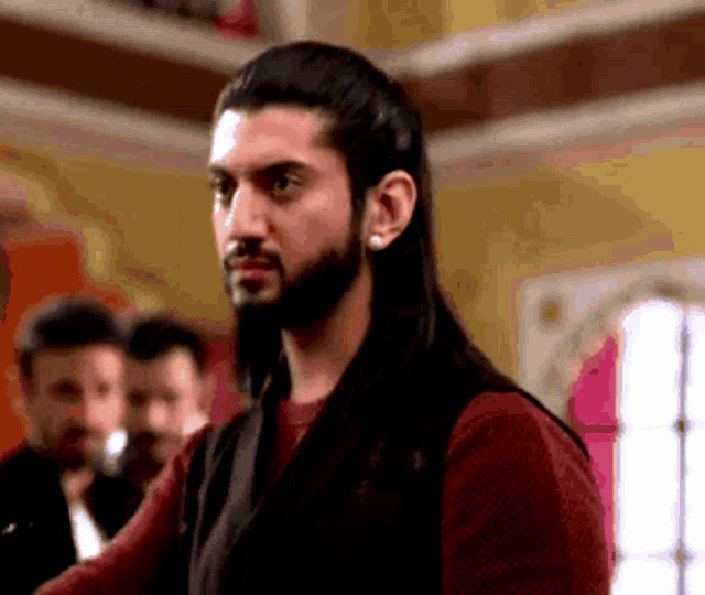 a man with long hair and a beard is wearing earrings and a red shirt .