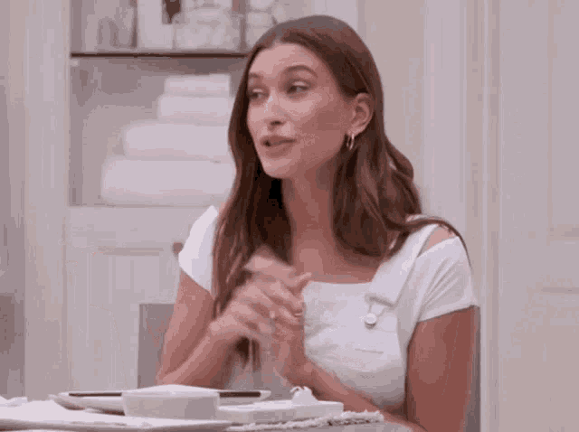 a woman in a white shirt is sitting at a table with a bowl of food and a plate of food .
