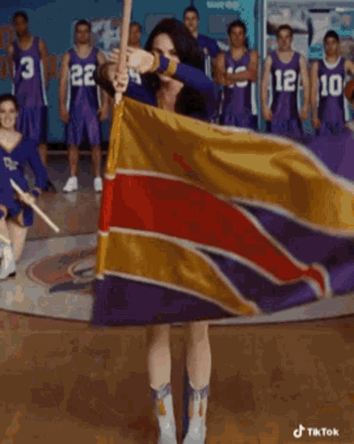 a cheerleader in a dk uniform is holding a flag in front of a basketball team .