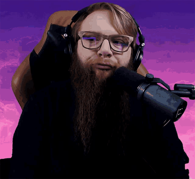 a man with a long beard wearing glasses and headphones stands in front of a microphone