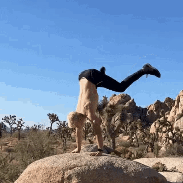 a man doing a handstand on top of a rock in the desert