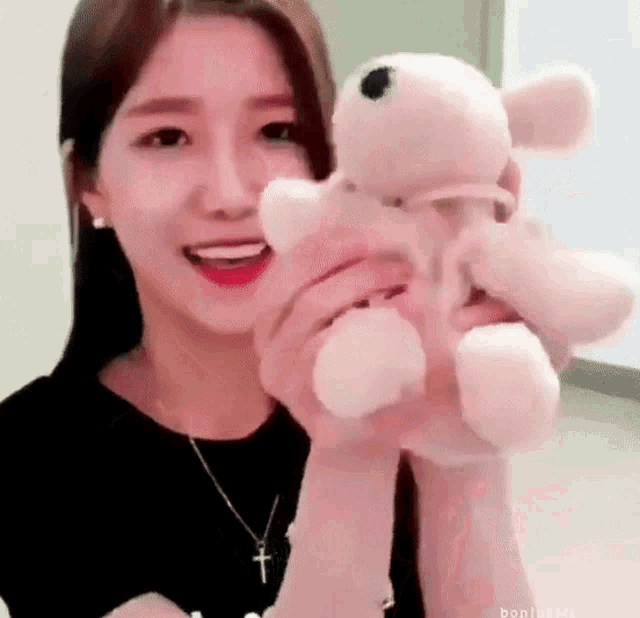 a young woman is holding a pink teddy bear in her hands .