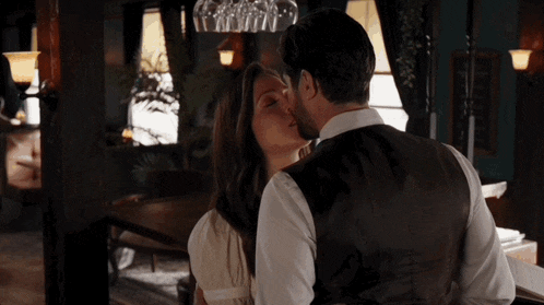 a man and woman are kissing in a room with wine glasses hanging from the ceiling