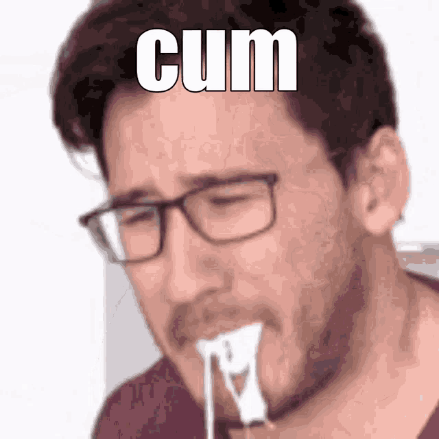 a man with glasses is eating a piece of cheese with the word cum written on his face .