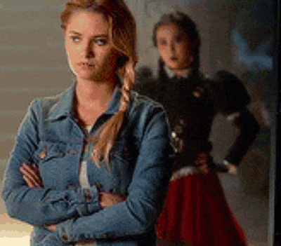 a woman in a denim jacket is standing with her arms crossed in front of a woman in a red dress .