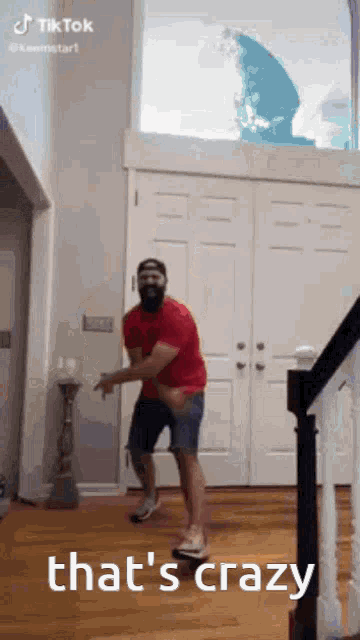 a man with a beard is dancing in a living room with stairs .