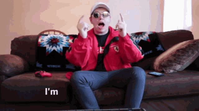 a man in a red jacket is sitting on a couch with the word i 'm in the corner