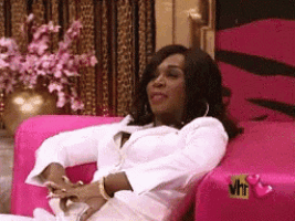 a woman in a white shirt is sitting on a pink couch with vh1 written on it .