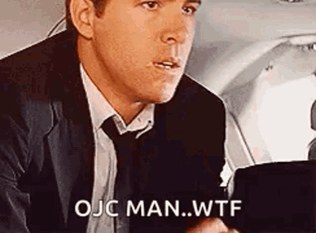 a man in a suit and tie is sitting in front of a laptop and says ojc man ... wtf .