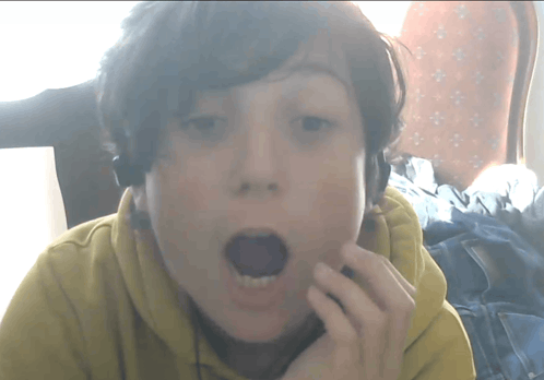 a young boy wearing headphones looks surprised with his mouth wide open