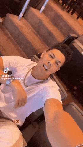 a man in a white shirt is taking a selfie while wearing a gold chain around his neck .