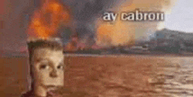 a man is standing in the water with a fire in the background and a burning building in the background .