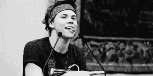 a young man wearing a bandana is sitting in front of a microphone and smiling .