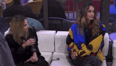 two women are sitting on a couch with a glass of wine