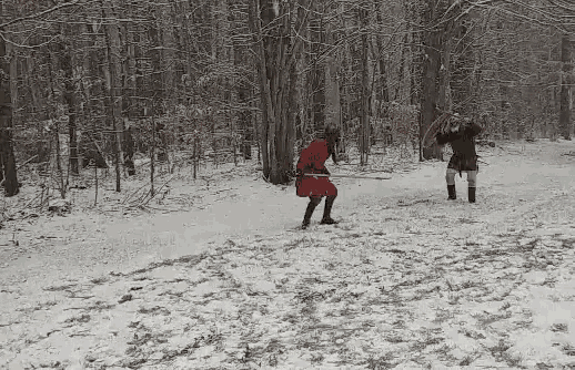 a man in a red dress is standing in the snow holding a sword .