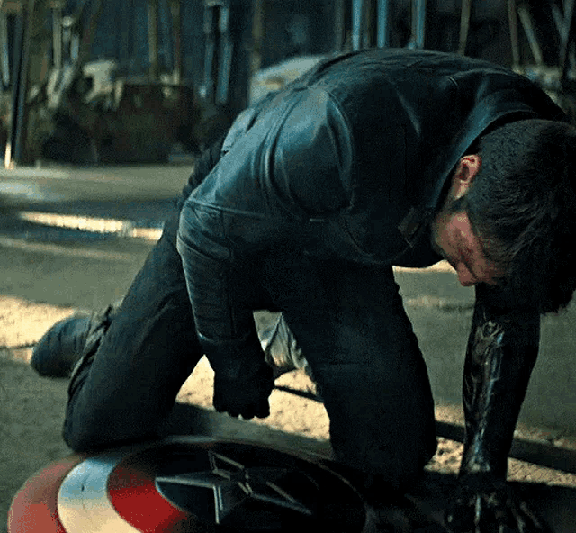 a man in a leather jacket is kneeling on a shield