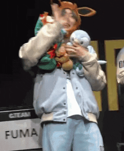 a man in a costume is holding a stuffed animal in front of a fuma sign