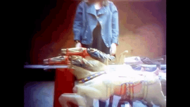 a woman in a denim jacket is standing in front of a carousel horse