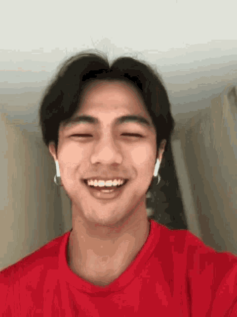 a young man wearing a red shirt and earrings is smiling .