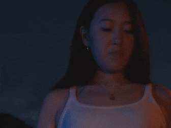 a woman wearing a white tank top and a necklace is standing in a dark room .
