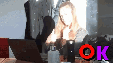 a woman is giving a thumbs up next to a laptop and a bottle of perfume
