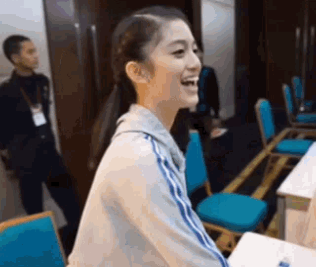 a woman is sitting at a table in a room with blue chairs and smiling .