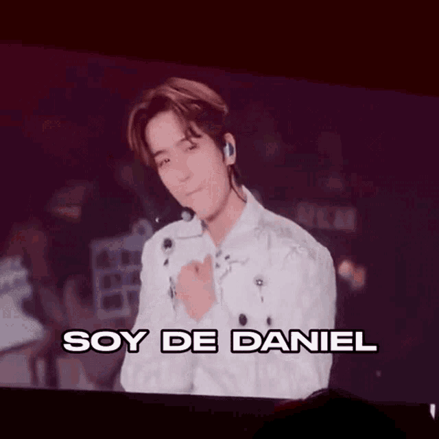 a man in a white shirt is standing in front of a large screen that says soy de daniel