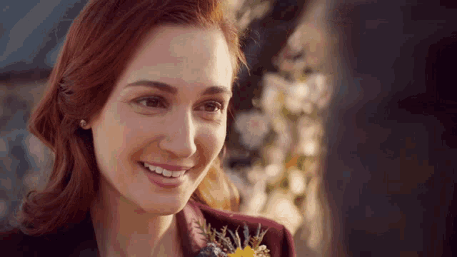 a woman with red hair is smiling while holding a flower