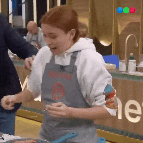 a woman wearing a masterchef apron is cooking in a kitchen