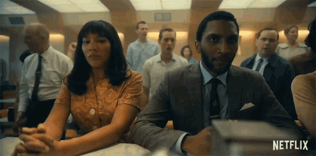 a man and a woman are sitting at a table with their hands folded in front of a crowd .