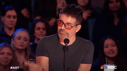 a man wearing glasses is speaking into a microphone in front of a crowd of people with a nbc cup in front of him
