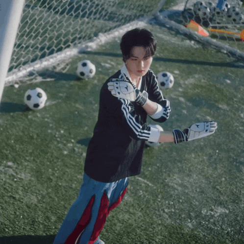 a man wearing a black adidas shirt and gloves stands on a soccer field surrounded by soccer balls