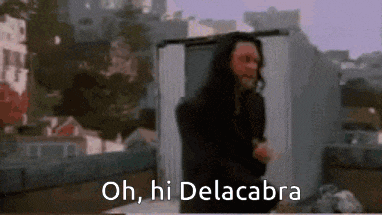 a man with long hair is standing on a roof with the words oh , hi dela cabra written below him .