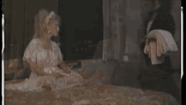 a woman in a white dress sits on a bed with a maid