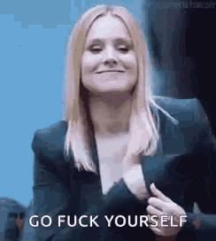 a woman in a suit is giving a thumbs up and smiling while saying `` go fuck yourself '' .