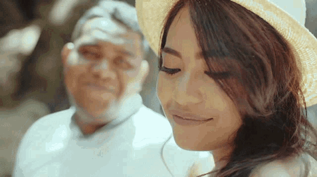 a woman wearing a straw hat is smiling while standing next to a man