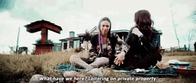a couple of women are sitting on a blanket in the grass .