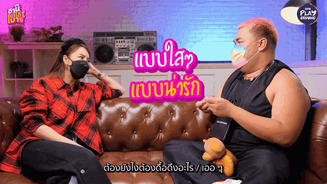 a man and a woman wearing face masks are sitting on a couch with a sign that says play online in the background