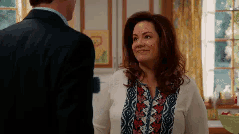 a man and a woman are looking at each other in a kitchen and the woman is smiling .