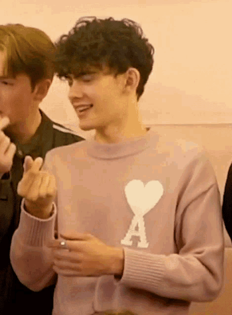 a young man wearing a pink sweater with the letter a and a heart on it
