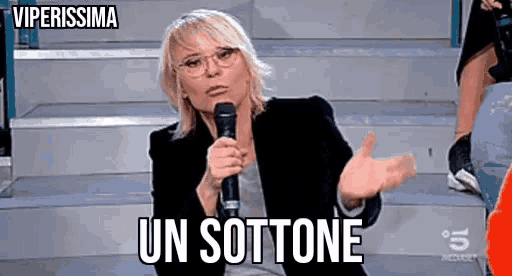 a woman is holding a microphone and talking into it while wearing glasses .
