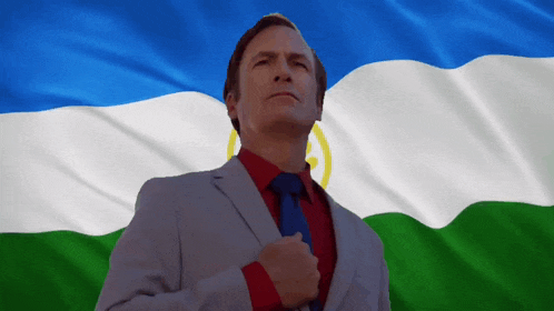 a man in a suit and tie stands in front of a blue and green flag