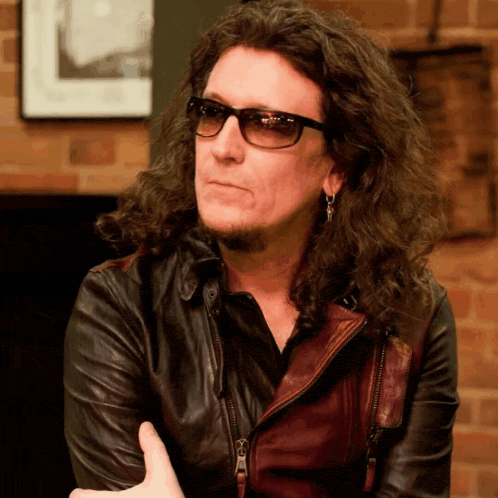 a man with long curly hair wearing a leather jacket and sunglasses