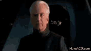 a man with gray hair and a black shirt is sitting in a dark room .