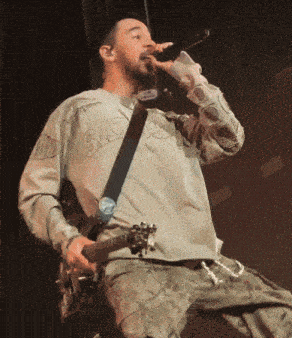 a man singing into a microphone while holding a guitar and wearing a shirt that says saturday