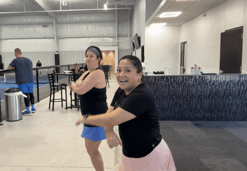 two women are dancing in a gym and one is wearing a black tank top
