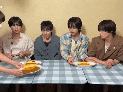 a group of young men are sitting at a table with plates of food and one of them is wearing a shirt that says 13 on it
