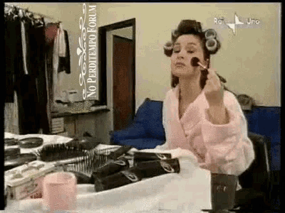 a woman with curlers in her hair is applying makeup in front of a mirror with a sign that says no perditempo forum on it