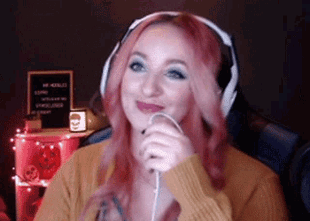 a woman wearing headphones and a yellow sweater is holding a microphone and smiling .